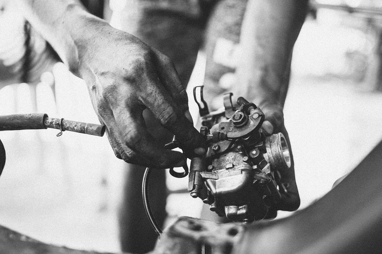 A mechanic's hands working on a carburettor, in black and white